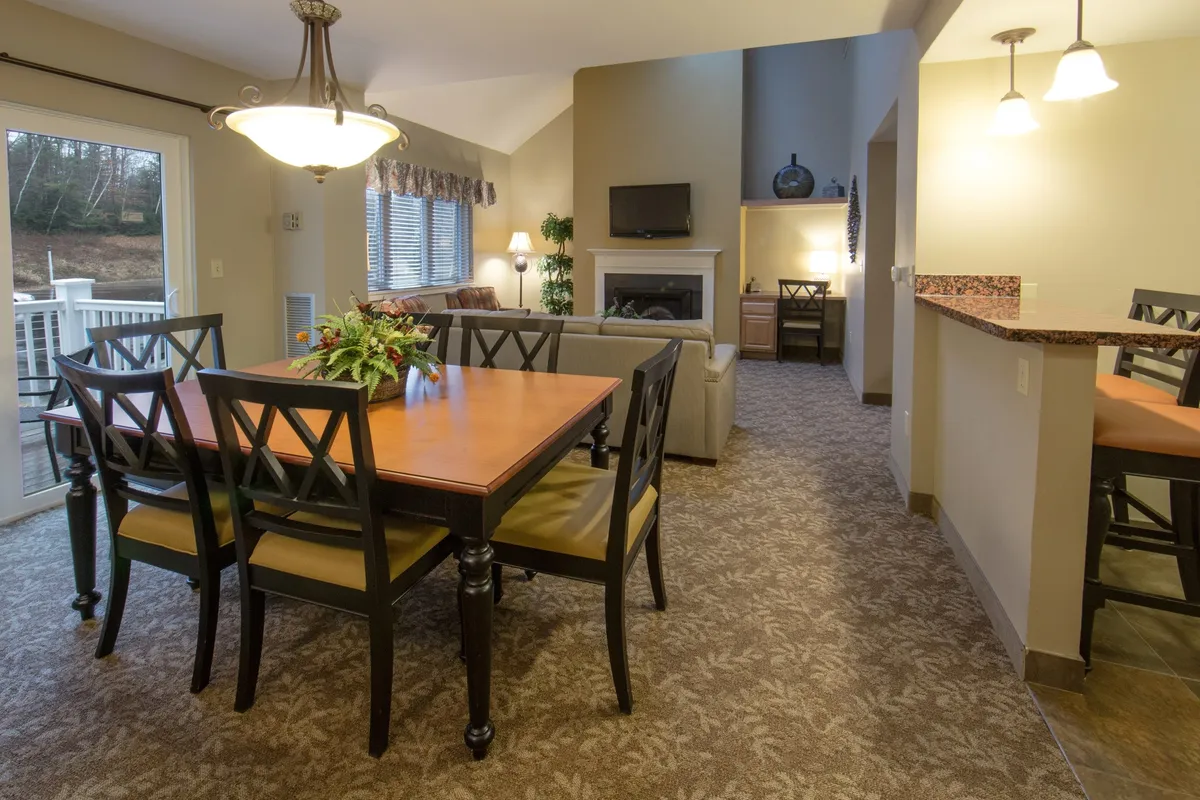 This interior image features a welcoming open-concept living and dining area. The focal points include a plush living room seating arrangement positioned around a fireplace and a nearby dining table. The space is illuminated with warm light, inviting guests to gather for meals, socializing, or relaxing by the fire after a day out.