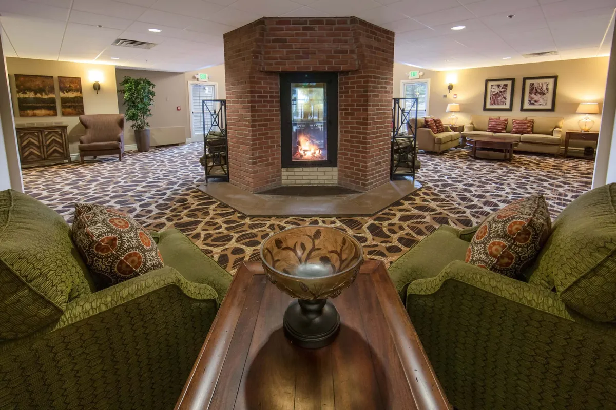 This image centers on a living area anchored by a central fireplace, surrounded by green upholstered chairs and textured flooring, with a decorative bowl adding a personalized touch. The arrangement suggests a cozy, communal space ideal for reading, conversation, or simply enjoying the fire.