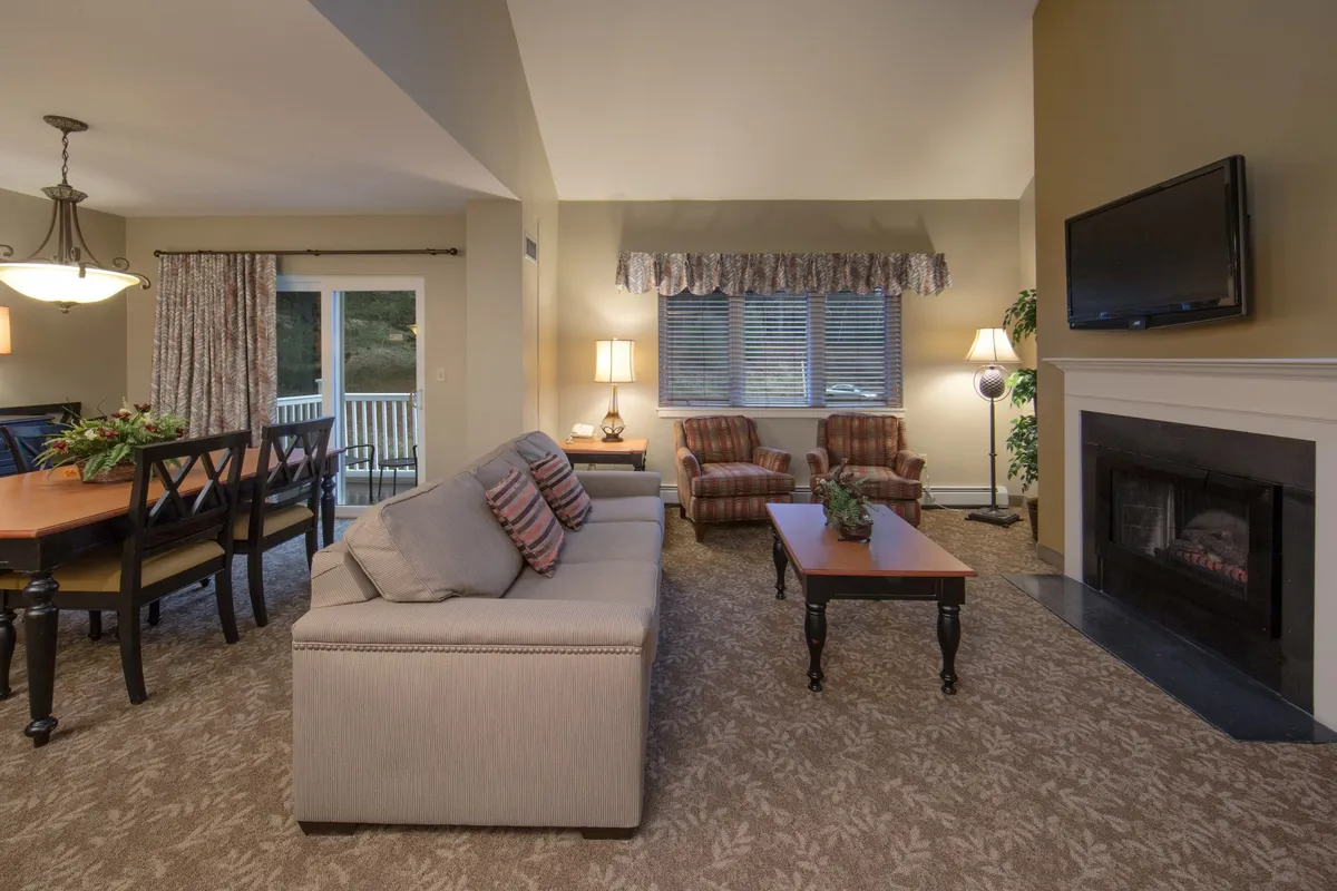 The image showcases a warm, inviting living and dining space with a plush sofa, a dining table set for gatherings, a glowing fireplace, and large windows with elegant curtains, all designed for comfort and togetherness.