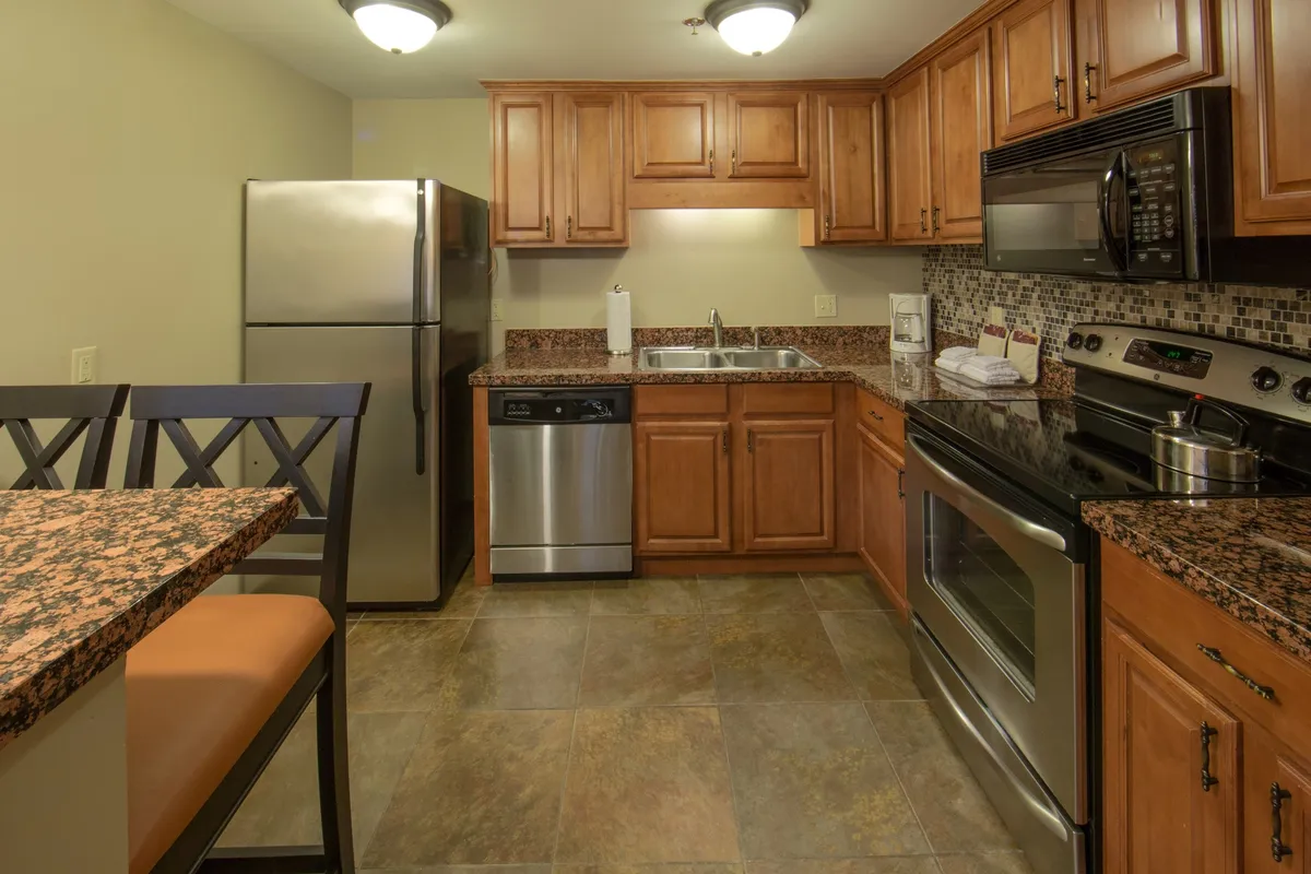 A spacious kitchen and dining area featuring a granite countertop, stainless steel appliances, and wood cabinets. Bar seating allows for casual meals or sipping coffee while chatting. The warm lighting and inviting decor create a welcoming atmosphere for cooking, socializing, and celebrating special occasions.